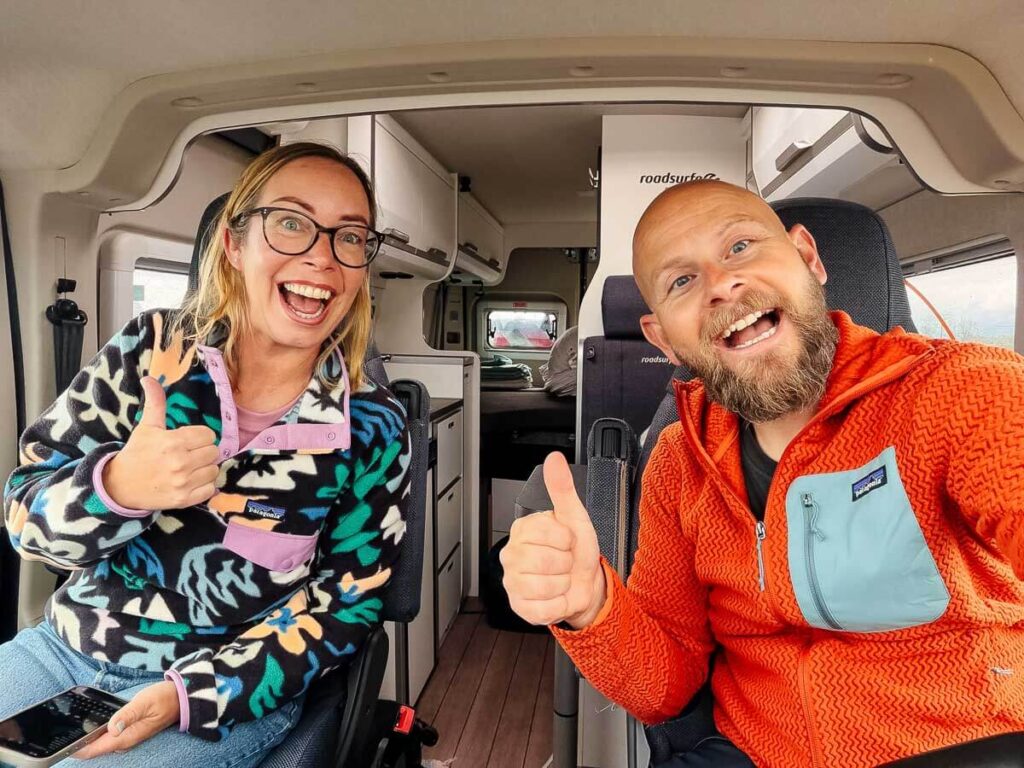 Couple smiling and giving thumbs up inside campervan interior