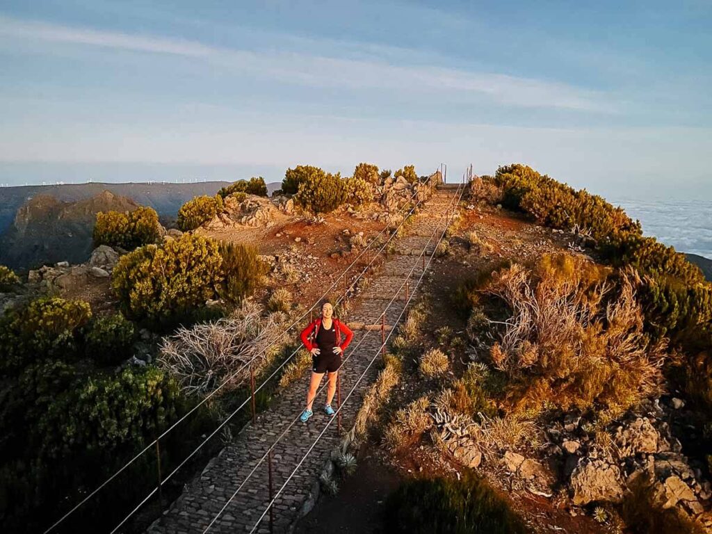 Hiker on a scenic mountain trail at sunset with lush greenery