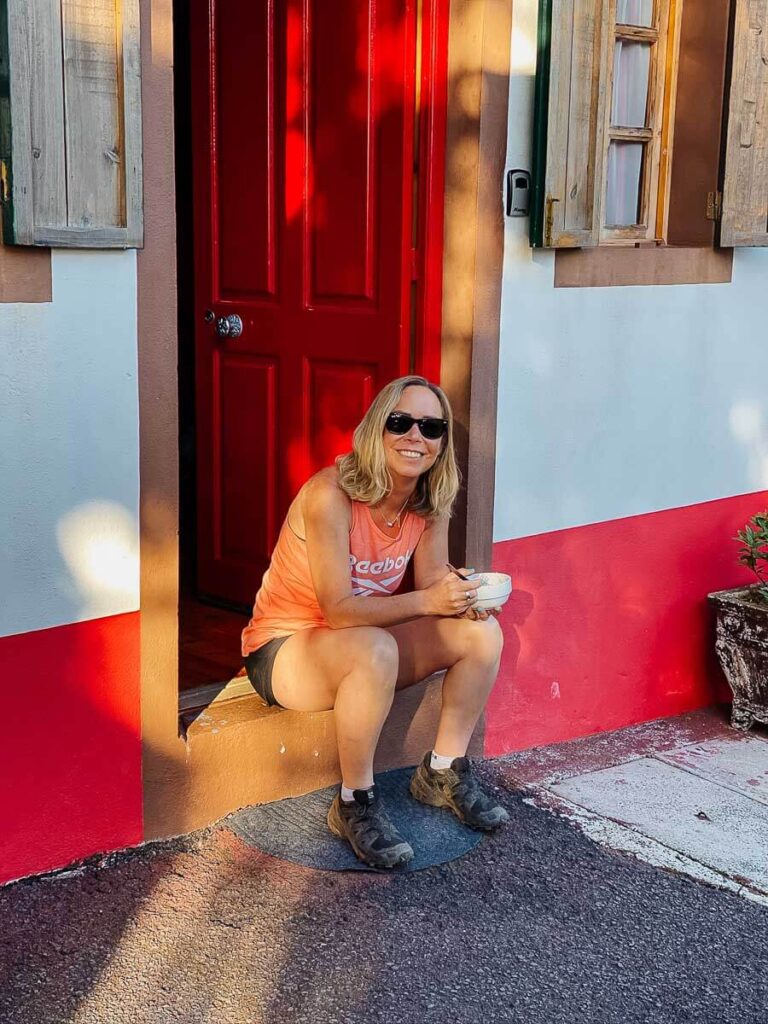 Woman in sunglasses sitting by a bright red door holding a mug