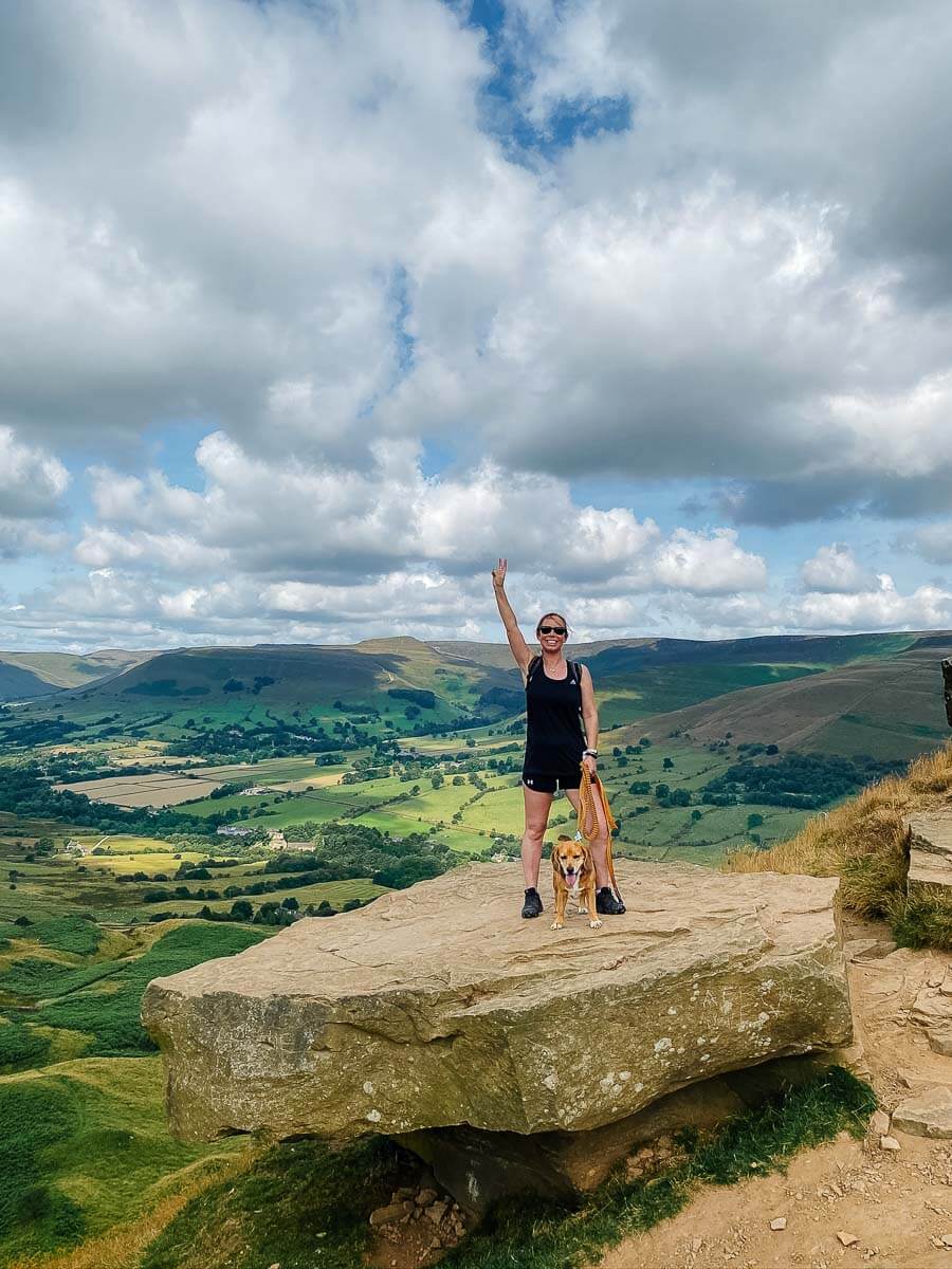 Hiker on a scenic hilltop with a dog under a cloudy sky